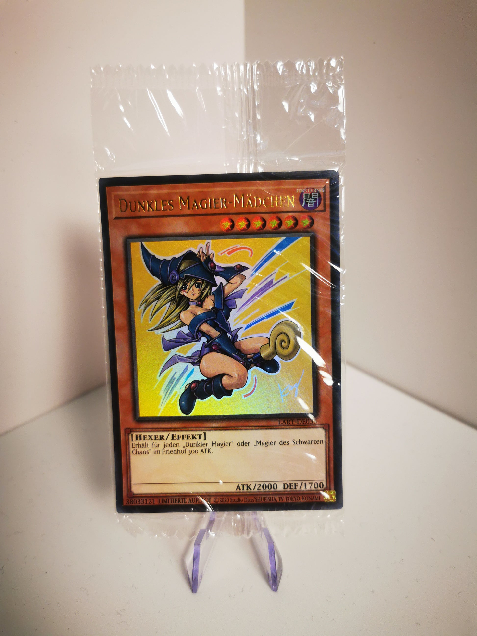 Vorderansicht der Yu-Gi-Oh! Karte Dunkles Magier-Mädchen LART-DE035 in Originalverpackung auf einem transparenten Kartenständer.